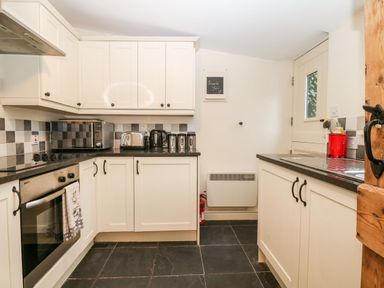 A kitchen with white cabinets black countertops a stove a toaster kettle and a microwave at White Lilac Cottage in Brynsiencyn