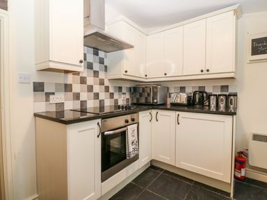 A kitchen with white cabinets black handles black countertop and black white checkered tile backsplash with oven microwave toaster kettle and canisters at White Lilac Cottage in Brynsiencyn