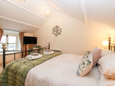 A bedroom with a metal framed bed pillows and towels a chair a television and a window at White Lilac Cottage Brynsiencyn