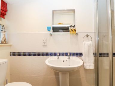 A bathroom with a toilet sink shower mirror and towel at White Lilac Cottage in Brynsiencyn