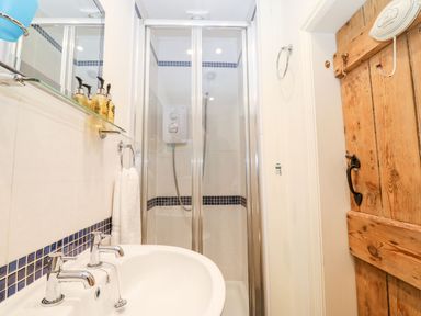 A bathroom with a sink and dual taps a glass shower enclosure and a wooden door at White Lilac Cottage in Brynsiencyn