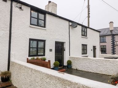 The exterior of a white textured cottage with black window frames bench and potted plants at White Lilac Cottage in Brynsiencyn
