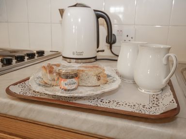 A kitchen counter with a kettle two white pitchers and a tray with scones and strawberry jam at Royal Oak Farm Cottage Betws-y-Coed