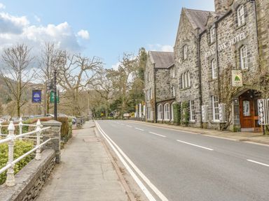 A street with stone buildings and a hotel named Royal Oak Hotel on the right side and a sidewalk with railings on the left side at Royal Oak Farm Cottage in Betws-y-Coed