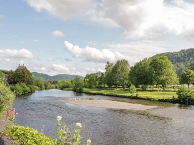 A river flowing through a landscape with trees on the banks and hills in the background at Royal Oak Farm Cottage in Betws-y-Coed