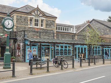 A stone building with blue framed windows and doors with a clock and bike outside in Betws-y-Coed