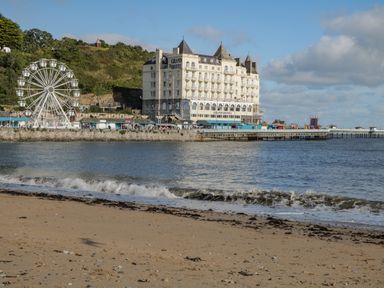 A beach with waves near a pier and a large building labeled grand hotel with a ferris wheel nearby