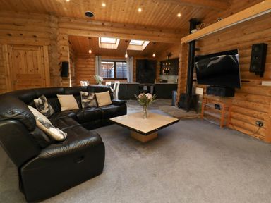 A living room with a black leather sofa a square coffee table with flowers a wall-mounted TV and a kitchen area at Starwood in Felton