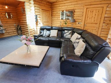 A living room with a black leather sectional sofa and a square coffee table with flowers in a log cabin at Starwood Felton