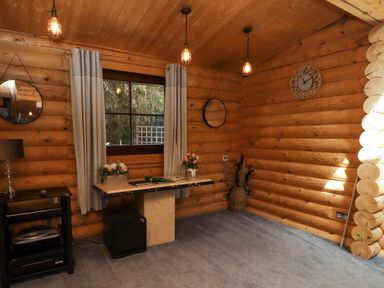 A wooden log cabin room with a window curtains table flowers hanging mirrors and a wall clock at Starwood in Felton
