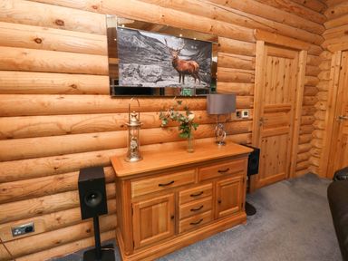 A wooden sideboard with a lamp a vase with flowers and a lantern in a log cabin room with two wooden doors and speakers at Starwood in Felton