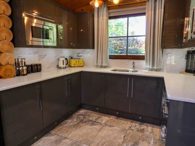 A kitchen with dark cabinets a microwave a yellow toaster a kettle mugs and a window with curtains at Starwood in Felton