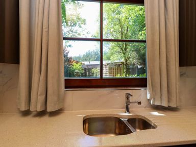 A kitchen sink with a chrome faucet under a window with beige curtains at Starwood in Felton