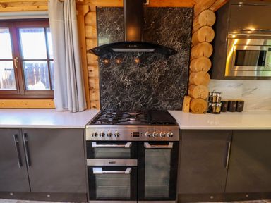 A kitchen with a double oven and gas stove under a black range hood between grey cabinets with a window on the left and a microwave on the right at Starwood in Felton