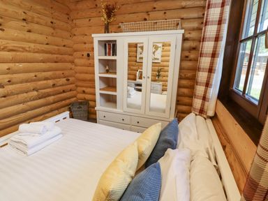 A bedroom with a bed with pillows and folded towels next to a white cabinet with mirrored doors and shelves in a log cabin at Starwood in Felton