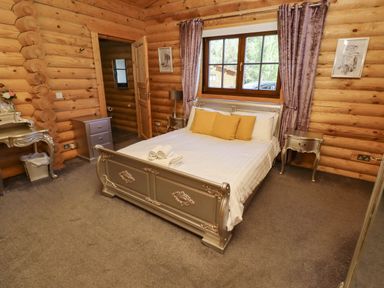 A bedroom with a silver bed frame white bedding yellow pillows a window with curtains and wooden log walls at Starwood in Felton
