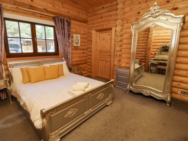 A bedroom with a bed with yellow pillows a large ornate mirror and wooden log walls at Starwood in Felton