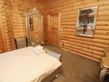 A bedroom with a bed folded towels a large ornate mirror a wooden door a silver nightstand and a framed picture on a log wall at Starwood in Felton
