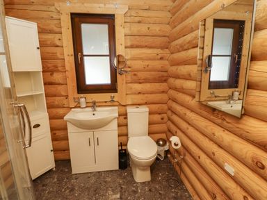 A bathroom with a toilet sink cabinet mirror and storage unit with log walls at Starwood in Felton