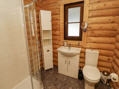 A bathroom with a shower enclosure a white sink cabinet a white toilet a tall white storage cabinet and a window with wooden frame at Starwood in Felton