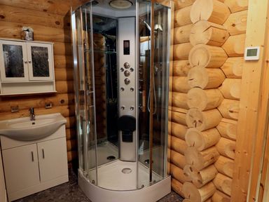 A bathroom with a glass shower cabin and a white sink cabinet in a log cabin style room at Starwood in Felton