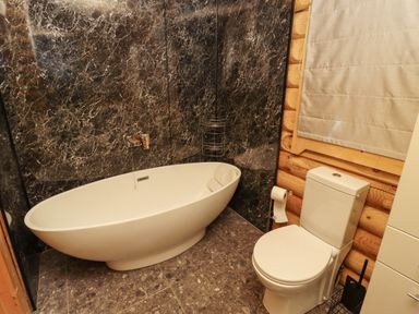 A bathroom with a white bathtub and toilet set against black marble and wooden walls at Starwood in Felton