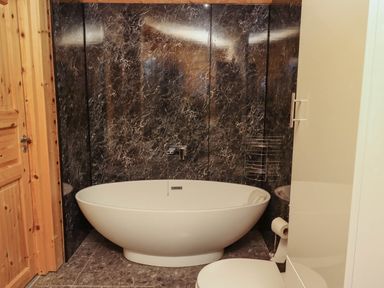 A bathroom with an oval bathtub black marble wall and wooden door at Starwood in Felton