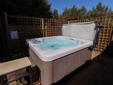 An outdoor hot tub with water inside and a cover partially open surrounded by wooden lattice fencing at Starwood in Felton