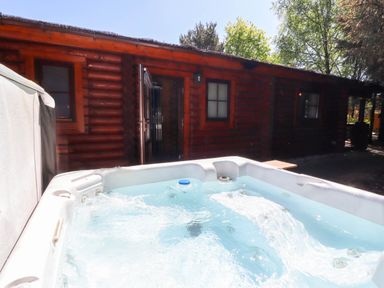 An outdoor hot tub with bubbling water in front of a wooden cabin surrounded by trees at Starwood in Felton