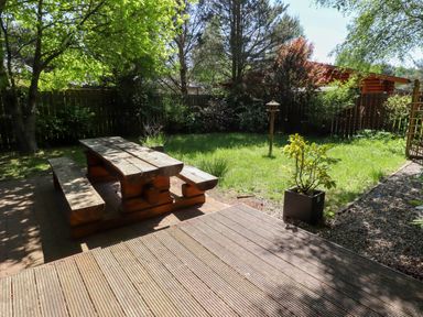 A wooden picnic table and benches in a backyard with grass trees plants and a bird feeder at Starwood in Felton
