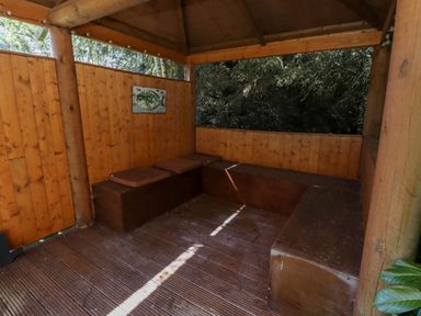 A wooden gazebo with built-in benches and cushions surrounded by trees at Starwood Felton