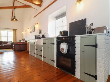 A kitchen with wooden floor green cabinets black oven and living area with brown leather sofas at Joes Barn in Mullion