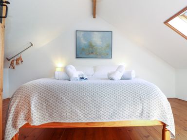 A bedroom with a double bed with rolled towels and a painting on the wall at Joe's Barn in Mullion