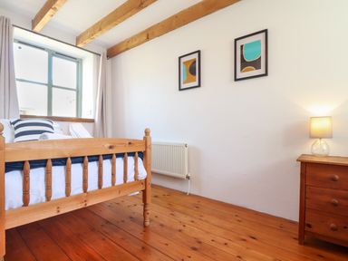 A bedroom with a wooden bed frame two framed pictures on the wall a wooden nightstand with a lamp and wooden floor at Joes Barn in Mullion