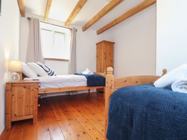 A bedroom with two single beds wooden floors a small wooden bedside table a wooden wardrobe and a window at Joes Barn in Mullion
