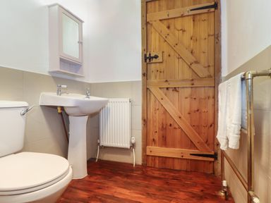 A bathroom with a toilet sink wooden door and towel rack at Joes Barn in Mullion