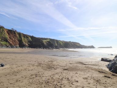 A sandy beach with footprints and rocky cliffs under a blue sky at Joe's Barn in Mullion