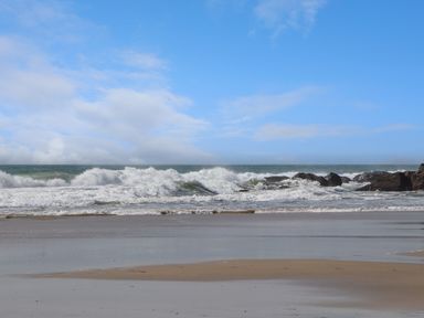 A sandy beach with ocean waves and rocks under a partly cloudy blue sky at Joe's Barn in Mullion