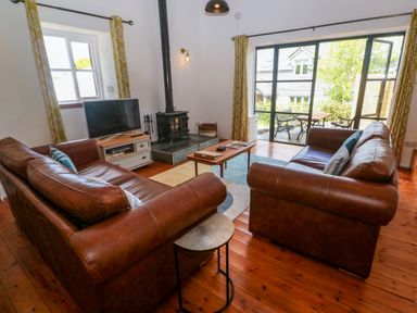 A living room with two brown leather sofas a wood stove a television and sliding glass doors leading to a garden at Joe's Barn in Mullion