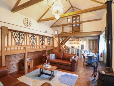 An open living room with brown leather sofas a wooden coffee table a rug and a kitchen with dining table and chairs at Berts Barn in Mullion