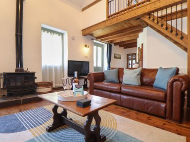 A living room with a leather sofa coffee table with wine and glasses wood stove and staircase at Berts Barn in Mullion
