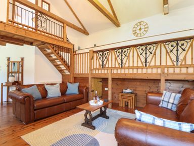 A living room with brown leather sofas a wooden coffee table and a staircase with wooden and metal railing at Berts Barn in Mullion