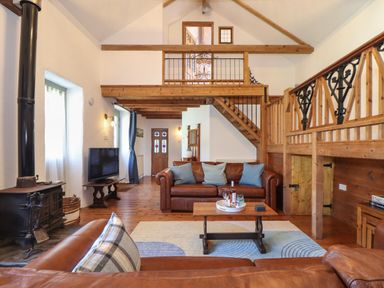 A living room with leather sofas wooden beams a wood burning stove a television and a balcony at Berts Barn in Mullion
