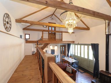 An open living area with wooden beams a dining table a leather chair large chandelier and green double doors at Berts Barn in Mullion