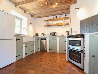 A kitchen with wooden floor green cabinets white walls and a stainless steel oven at Berts Barn in Mullion