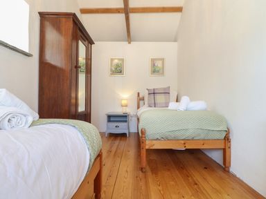 A bedroom with two single wooden beds green bedding a wooden wardrobe and a nightstand with a lamp at Berts Barn in Mullion