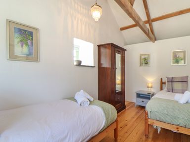 A bedroom with two single beds a wooden wardrobe a bedside table with a lamp and framed pictures on the walls at Berts Barn in Mullion