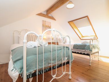 A bedroom with two single beds with white frames and blue blankets under a skylight window at Berts Barn in Mullion