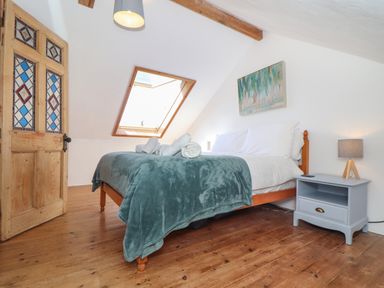 A bedroom with a double bed wooden floors stained glass door bedside table lamp and skylight window at Berts Barn in Mullion