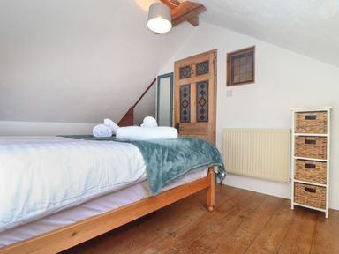 A bedroom with a wooden bed frame towels on the bed a wooden door a radiator and a storage unit with wicker baskets at Berts Barn in Mullion